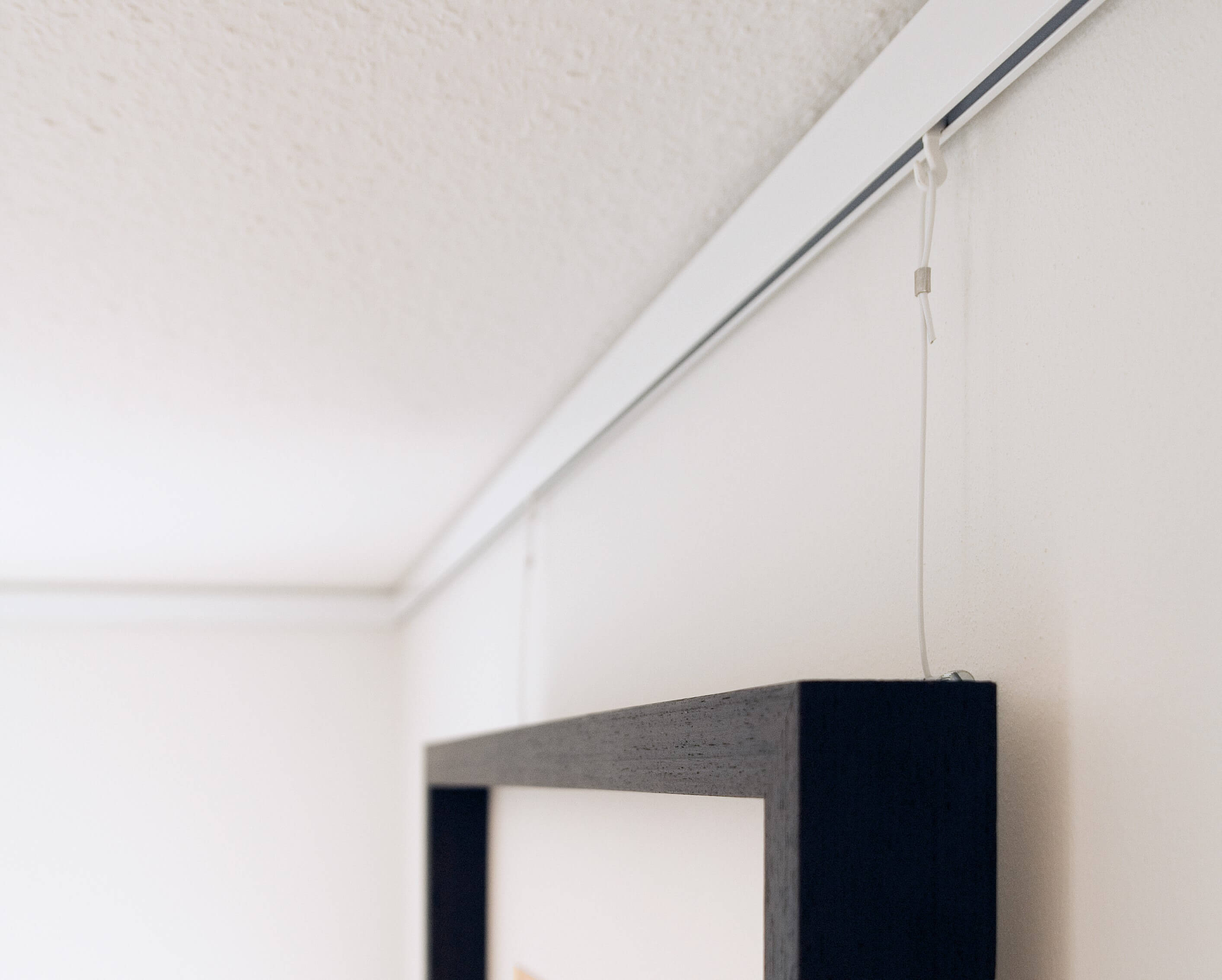 Eine Nahaufnahmer einer Galerischiene auf einer weißen Wand mit einem schwarzen Rahmen